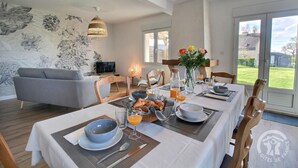 A dining area with a table set for breakfast, including croissants and orange juice, in a modern room with a large window and a floral wall mural. - Le Rocher - Trelivan (TRELIVAN)