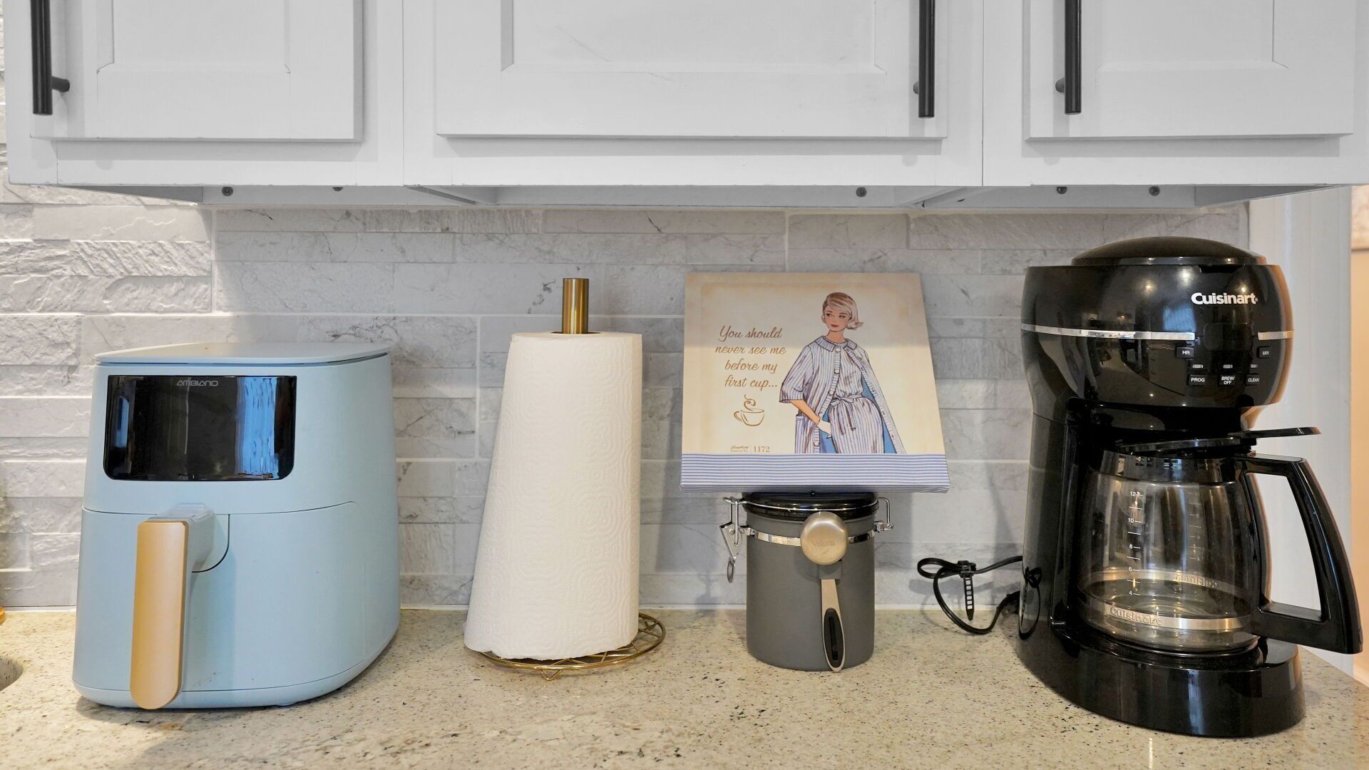 A kitchen with a coffee maker, a paper towel dispenser, and a framed picture on the counter.