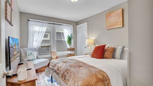 Une chambre à coucher avec un lit, une table de chevet, une lampe et une fenêtre avec des rideaux.