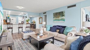 A living room with a sofa, coffee table, and chairs. There is a kitchen area in the background with a refrigerator and a sink. - Golf/Water View Condo
 (Sarasota)