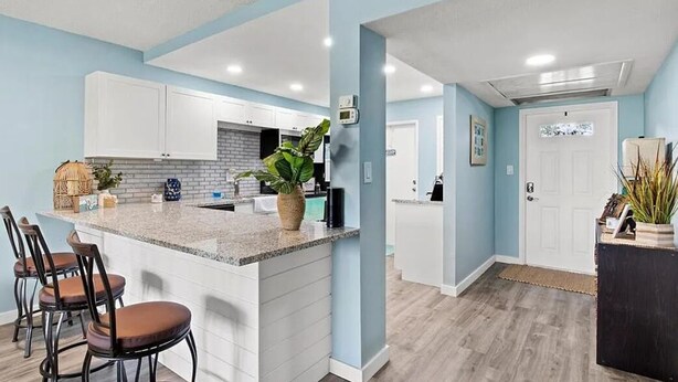 A modern kitchen with white cabinets, a granite countertop, and a central island with bar stools. - Golf/Water View Condo
 (Sarasota)