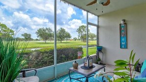 A balcony with a view of a green landscape, a 'WELCOME' sign, and a table with a lantern. - Golf/Water View Condo
 (Sarasota)