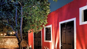 A red building with a black door and windows, surrounded by plants and a tree. - Villa Colonial en el Centro con Alberca (Mérida)
