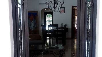 An open black wrought iron gate with a chandelier above, leading into a room with a tiled floor and a 'BIENVENIDO' mat.