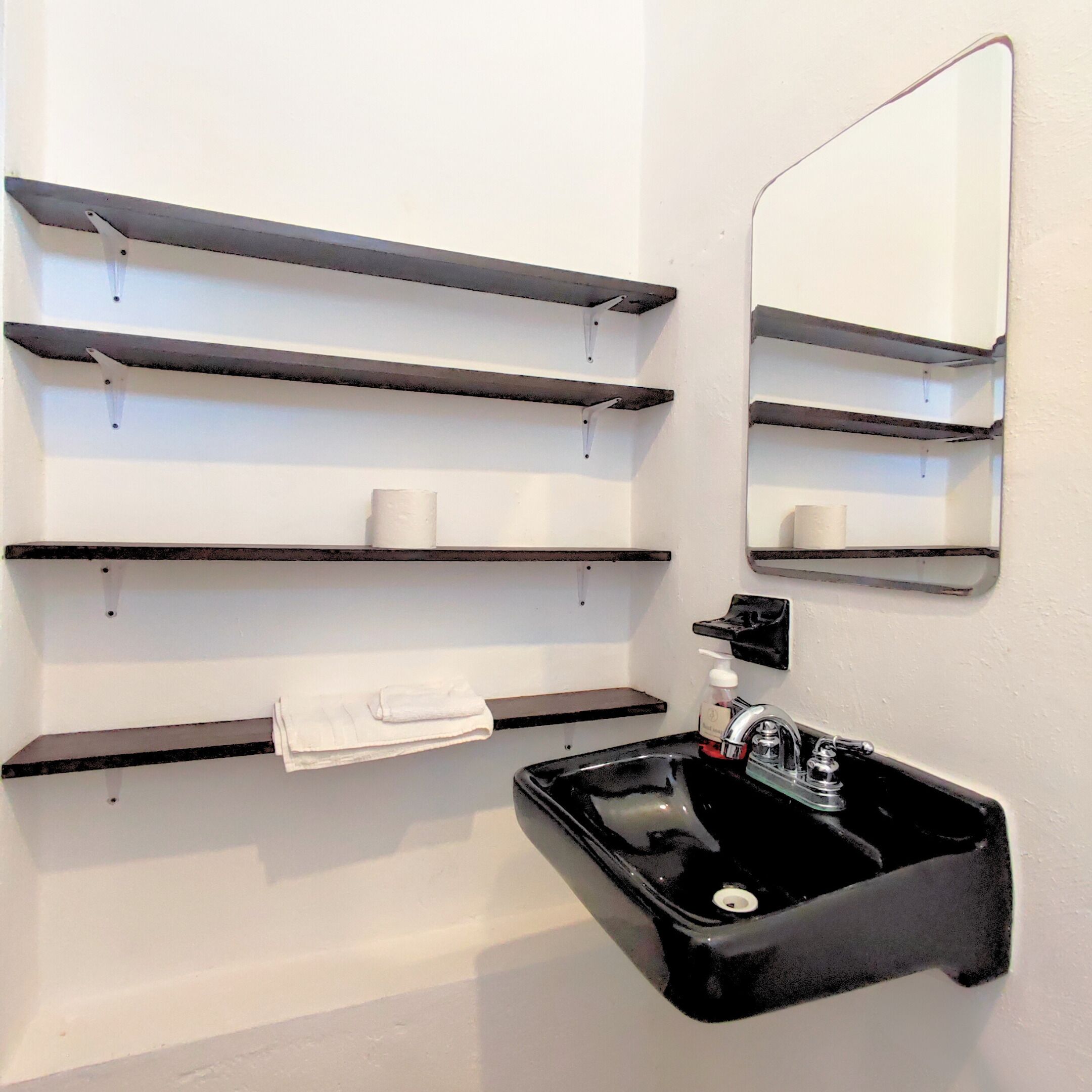 A bathroom with a black sink, a mirror, and multiple shelves for toiletries.