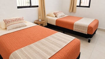 A hotel room with two beds, each with an orange quilt and a white throw. There are curtains on the windows, and a flat-screen TV mounted on the wall.