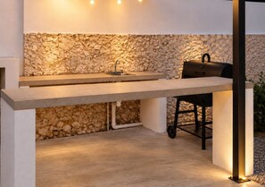 Un espace cuisine extérieur avec un mur en pierre en arrière-plan, un plan de travail et un barbecue.