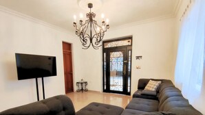 A living room with a large sectional sofa, a flat-screen TV, a chandelier, and a door leading outside. - Villa Colonial en el Centro con Alberca (Mérida)