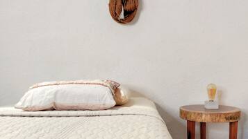A bedroom with a bed, pillows, a hanging decoration, and a small wooden table with a lamp.