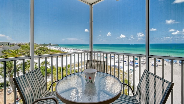 A balcony with a glass table and chairs, overlooking a beach with umbrellas and a clear blue sky. - Beachfront Condo - 2-Bedroom - Luxury - Directly on Crescent Beach (Siesta Key)
