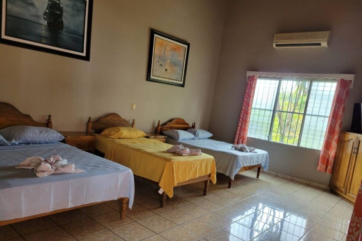 Una habitación con tres camas, una ventana con cortinas y un cuadro en la pared.