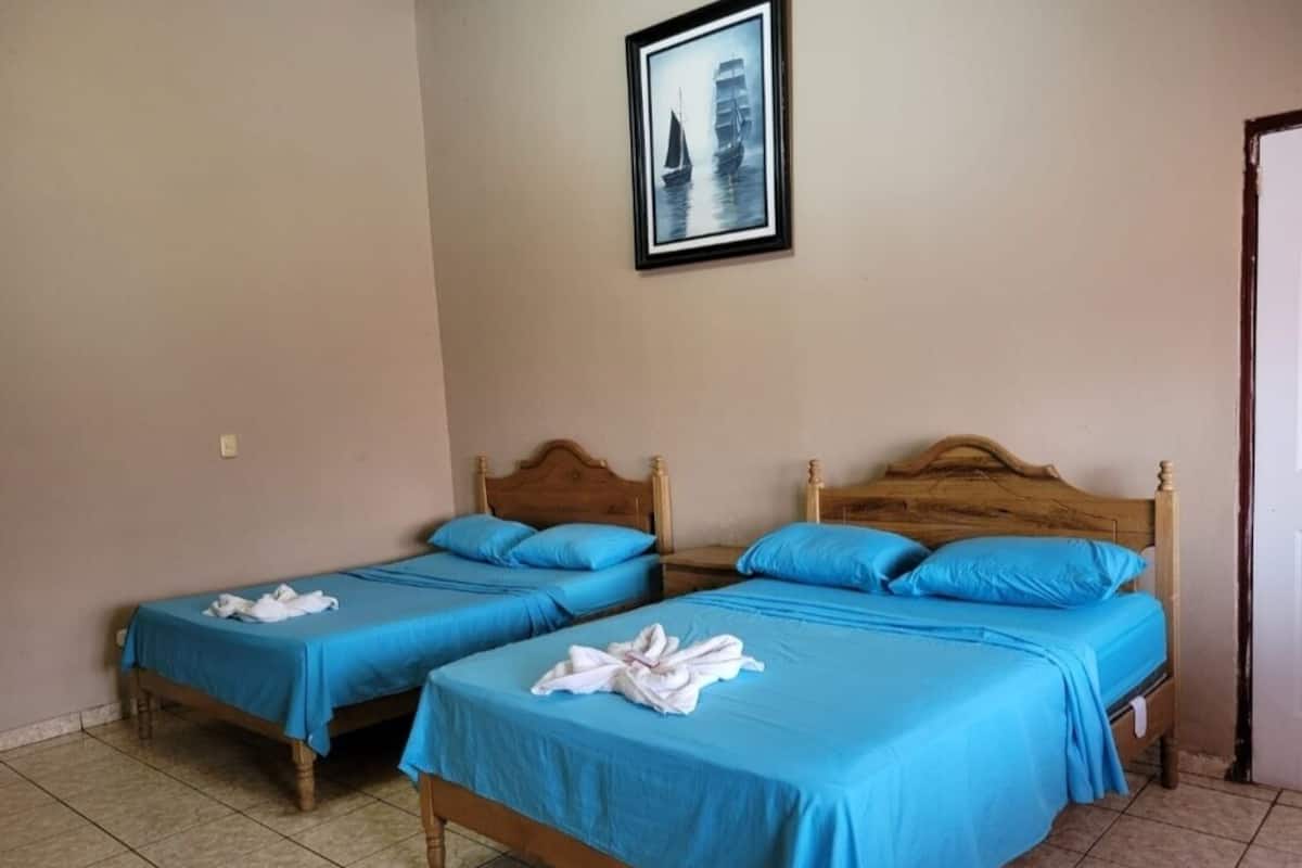 Dos camas individuales con ropa de cama azul, cabeceros de madera y un cuadro en la pared.