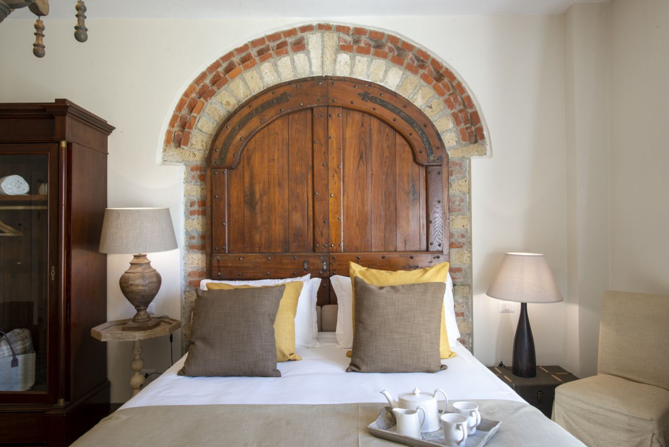 Hotelkamer met een groot houten hoofdeinde, een bed met witte lakens, twee bedlampjes en een dienblad met thee en bekers.