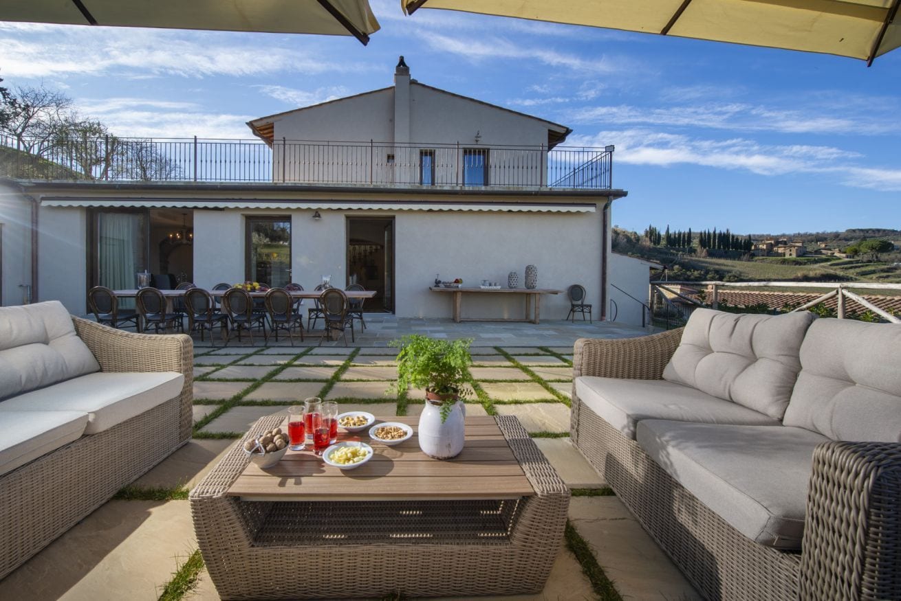 A patio area with wicker furniture, a table with drinks and snacks, and a view of a house with a balcony.