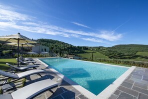 Una piscina con sillones de descanso y una pérgola, rodeada de campos en terrazas y un cielo despejado.