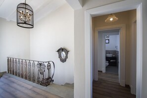 A staircase with ornate metal railings and a wall-mounted clock. A hallway leads to a bathroom with a sink and mirror. - MyExclusiveItaly - Villa Chianti with infinity pool and vineyard view (Greve in Chianti)