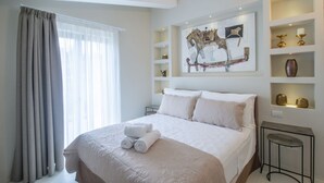 Ein Hotelzimmer mit einem großen Bett, einem Fenster mit Vorhängen, einer an der Wand befestigten Ablage mit Dekoration und einem kleinen Tisch.