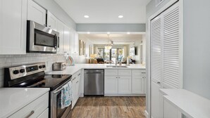 A modern kitchen with white cabinetry, stainless steel appliances, and a wooden floor. - Seashore Splendor with Ocean views, Heated Pool & Tennis Court (Cocoa Beach)