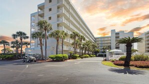 A multi-story hotel with balconies, palm trees, and a parking area. - Seashore Splendor with Ocean views, Heated Pool & Tennis Court (Cocoa Beach)