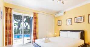 Habitación de hotel con una cama, puerta corredera de vidrio hacia una piscina y una pared con cuadros enmarcados.