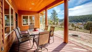 A wooden deck with a table and chairs, overlooking a forested landscape.