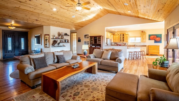 A spacious living area with wooden ceilings, a kitchen in the background, and a cozy seating arrangement.