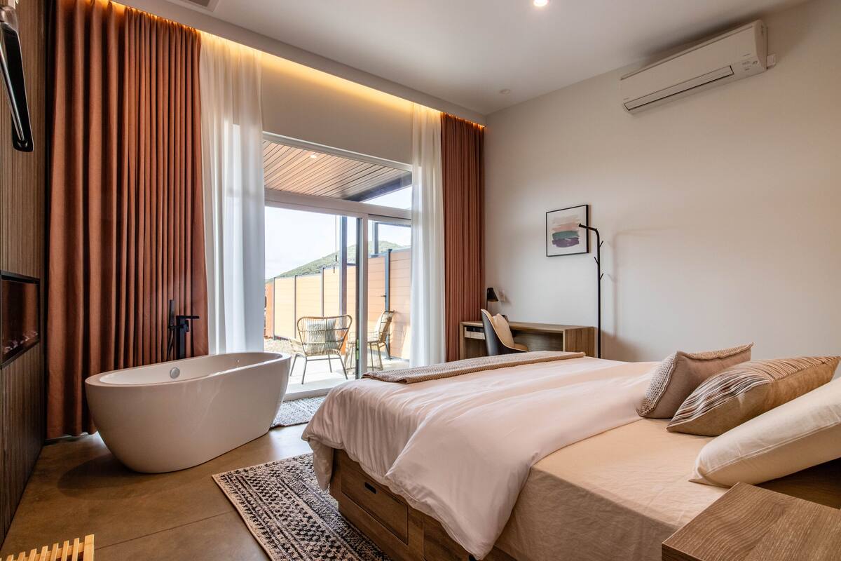 A modern bedroom with a large bed, a freestanding bathtub, and a desk with a chair.