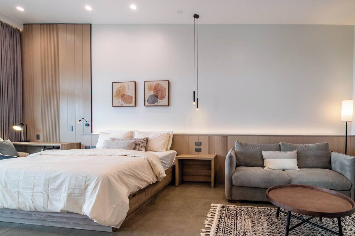 A modern hotel room with a bed, a sofa, a small table, and two wall-mounted light fixtures.