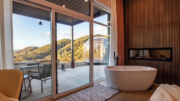 Ein modernes Badezimmer mit einer großen Badewanne, einer gläsernen Dusche und Blick auf eine Hügelterrasse.