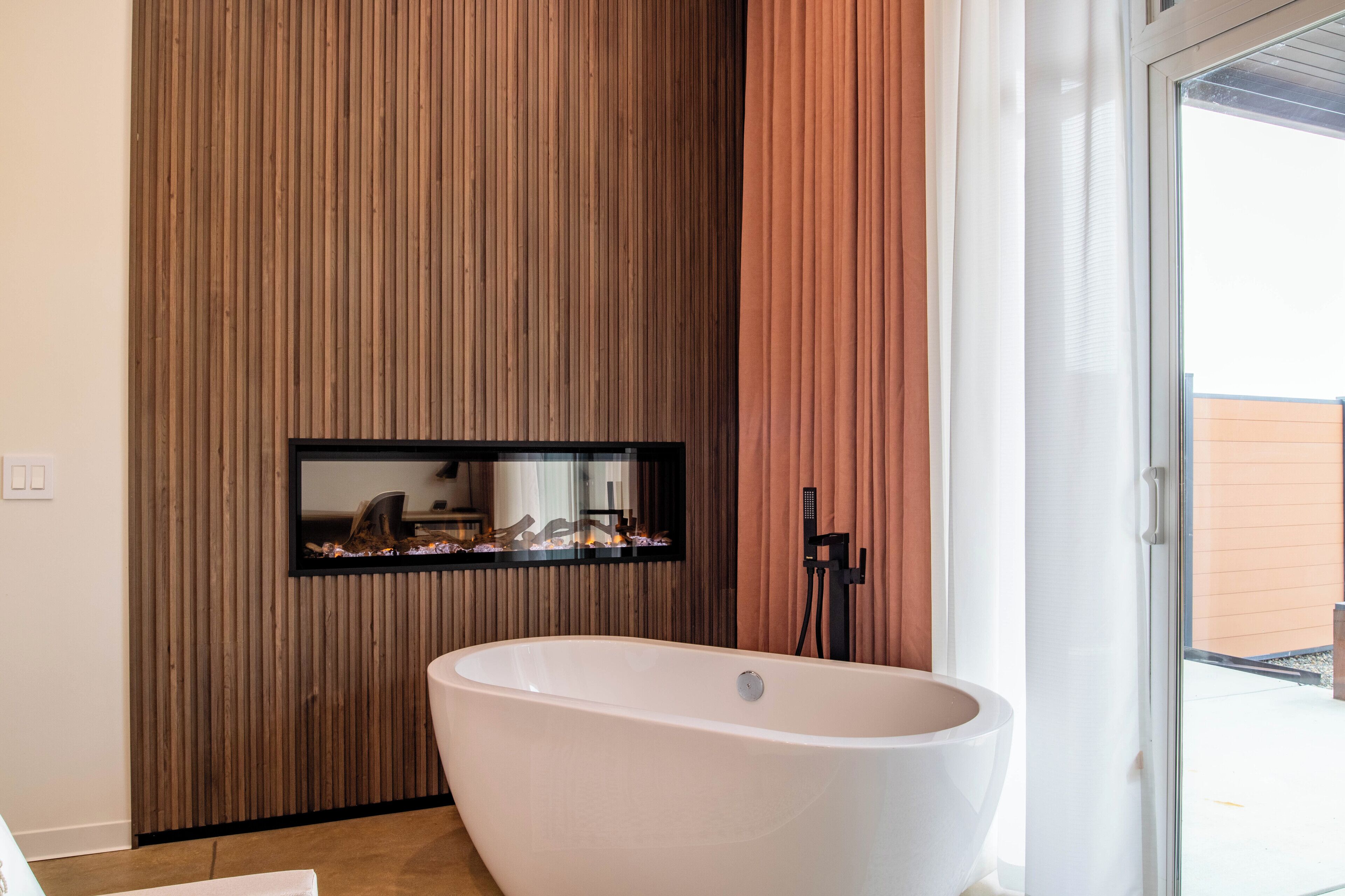 Ein modernes Badezimmer mit einer freistehenden Badewanne, Holzpaneelen, einem Spiegel und einem Fenster mit Aussicht.