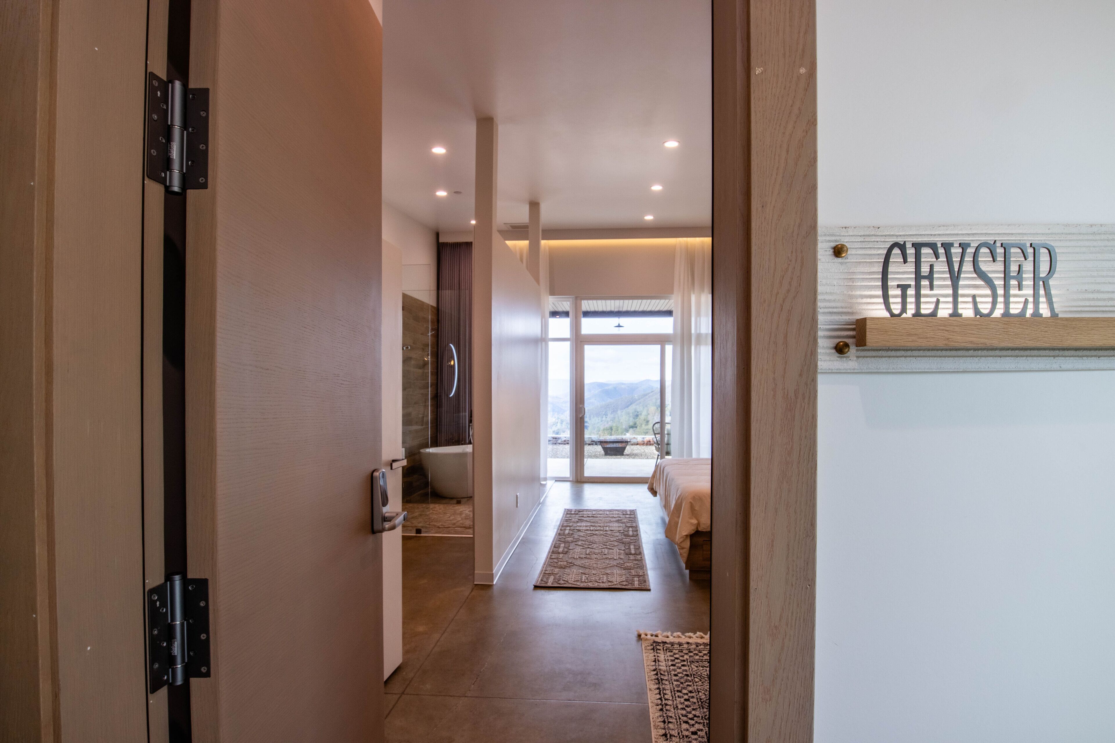 A hallway leading to a bedroom with a view, a bathroom, and a sign reading "GEYSER".