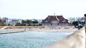 En byggnad vid kusten med en röd och vit fasad, belägen på en sandstrand med människor i bakgrunden.