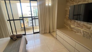 Habitació d'hotel moderna amb un llit gran, un televisor fixat a una paret de pedra i un balcó amb cortines.