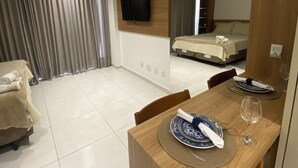 Una habitació d'hotel moderna amb zona de menjador, llit i televisió penjada a la paret.