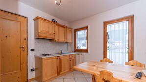 A kitchen with wooden cabinets, a marble countertop, and a dining table with chairs. - Casa Stella 4 (Falcade)