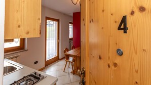 A kitchen with a stove, sink, and wooden cabinets. There is a dining area with a table and chairs. The room number is 4. - Casa Stella 4 (Falcade)