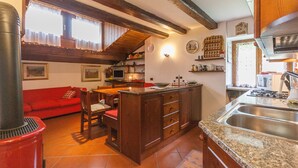 A kitchen with a central island, wooden beams, a red sofa, and a dining area. - Casa Silva (Falcade)