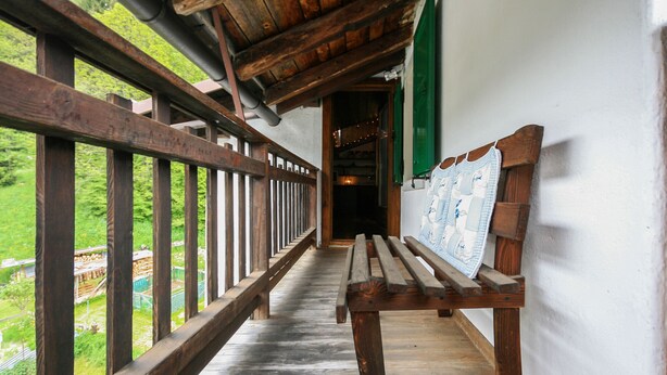 A wooden bench with a map on the backrest, a wooden railing, and a view of greenery outside. - Casa Silva (Falcade)