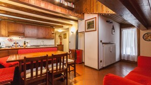 A cozy kitchen with wooden cabinets, a dining table with benches, and a red couch in a living area. - Casa Silva (Falcade)