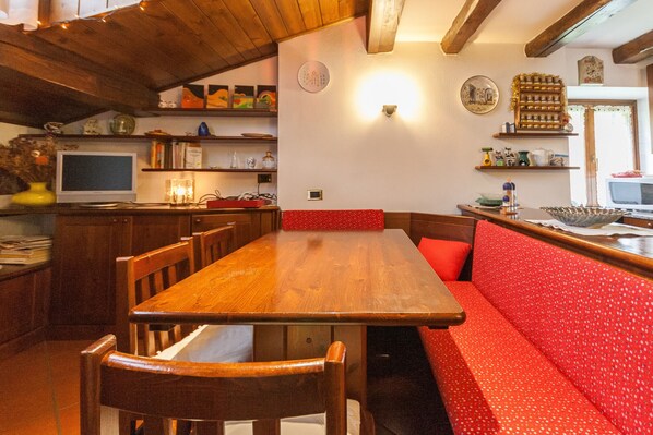 Een houten eettafel met stoelen, een rode gestoffeerde bank en een televisie op een plank.