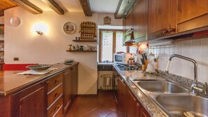 A kitchen with wooden cabinets, a granite countertop, a double sink, a stove, and a microwave. - Casa Silva (Falcade)