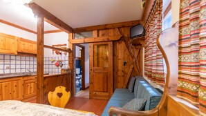 A rustic cabin interior with wooden walls, a kitchenette, a sofa, and a television. - Ski Residence 3B (Falcade)