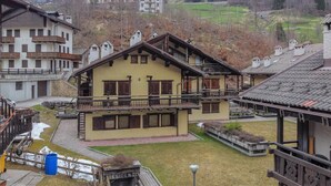 A traditional chalet-style building with a balcony, a stone facade, and a view of a hilly landscape. - Ski Residence 3B (Falcade)
