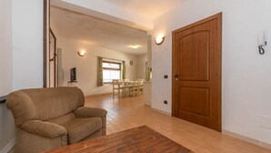 A living room with a sofa, a wooden coffee table, a dining area with a table and chairs, and a wooden door. - Villa Simona PT (Falcade)