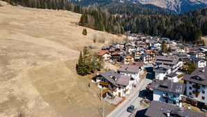 A mountainous village with traditional chalet-style buildings, a main road, and a clear view of the surrounding peaks. - Villa Simona PT (Falcade)
