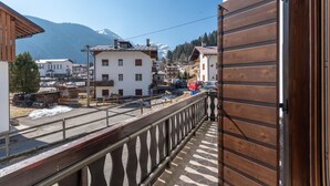 A balcony with a wooden railing overlooking a town with buildings and a mountain in the background. - Villa Simona PT (Falcade)