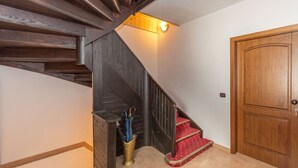 A wooden staircase with a red carpeted landing, a wooden door, and a brass umbrella holder. - Villa Simona PT (Falcade)