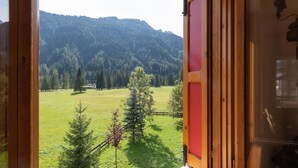 A room with a large window overlooking a green field and a forested mountain.