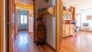 A wooden interior with a hallway leading to a room with a window, a wooden barrel, a bookshelf, and a television.
