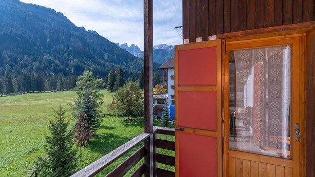 A wooden cabin with a red door and a balcony overlooking a mountainous landscape.